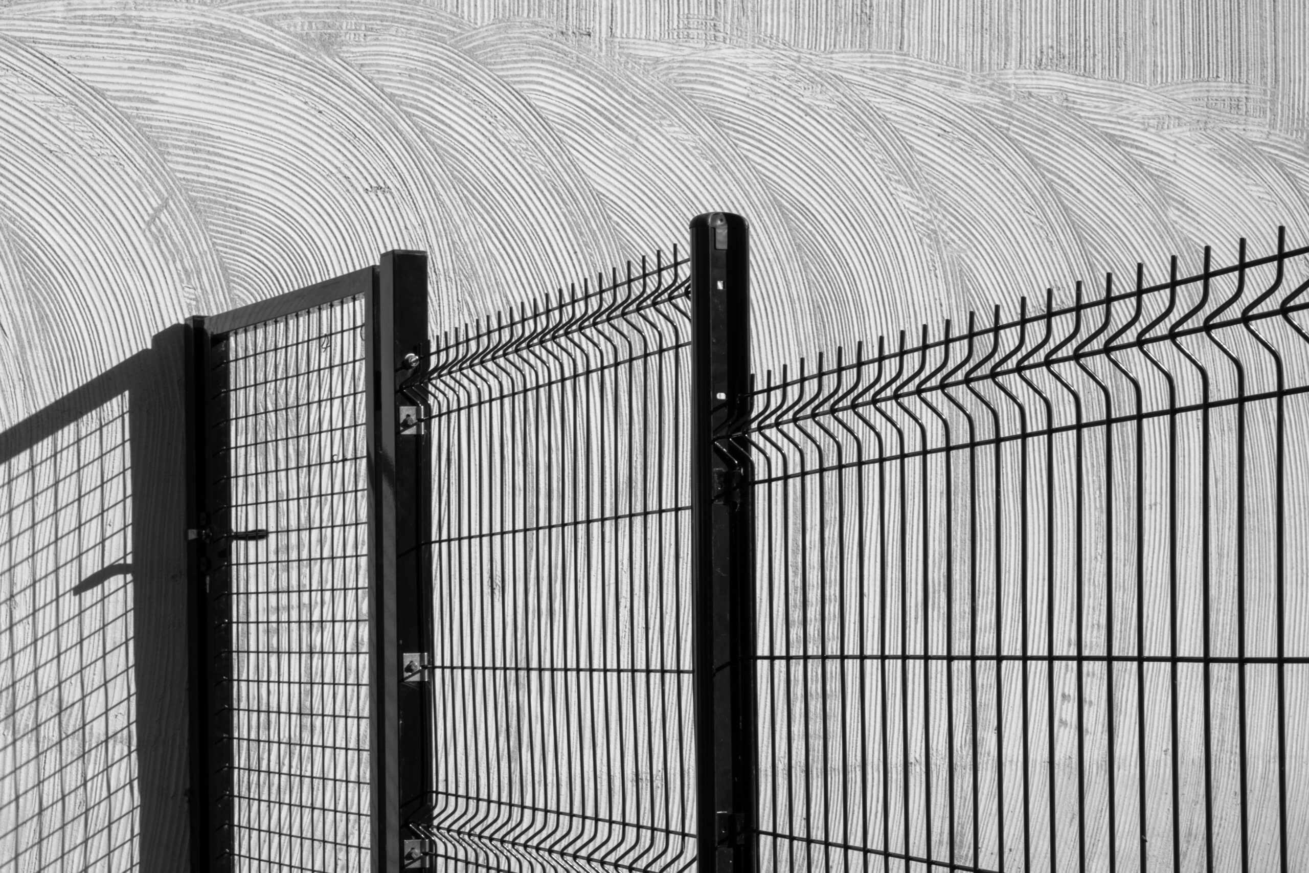 Teenused Artistic black and white photo of a wire fence casting shadows on a textured wall.